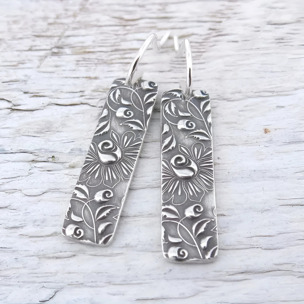 Silver retro geometric long strip carved vine earrings made from zinc alloy on a plain background