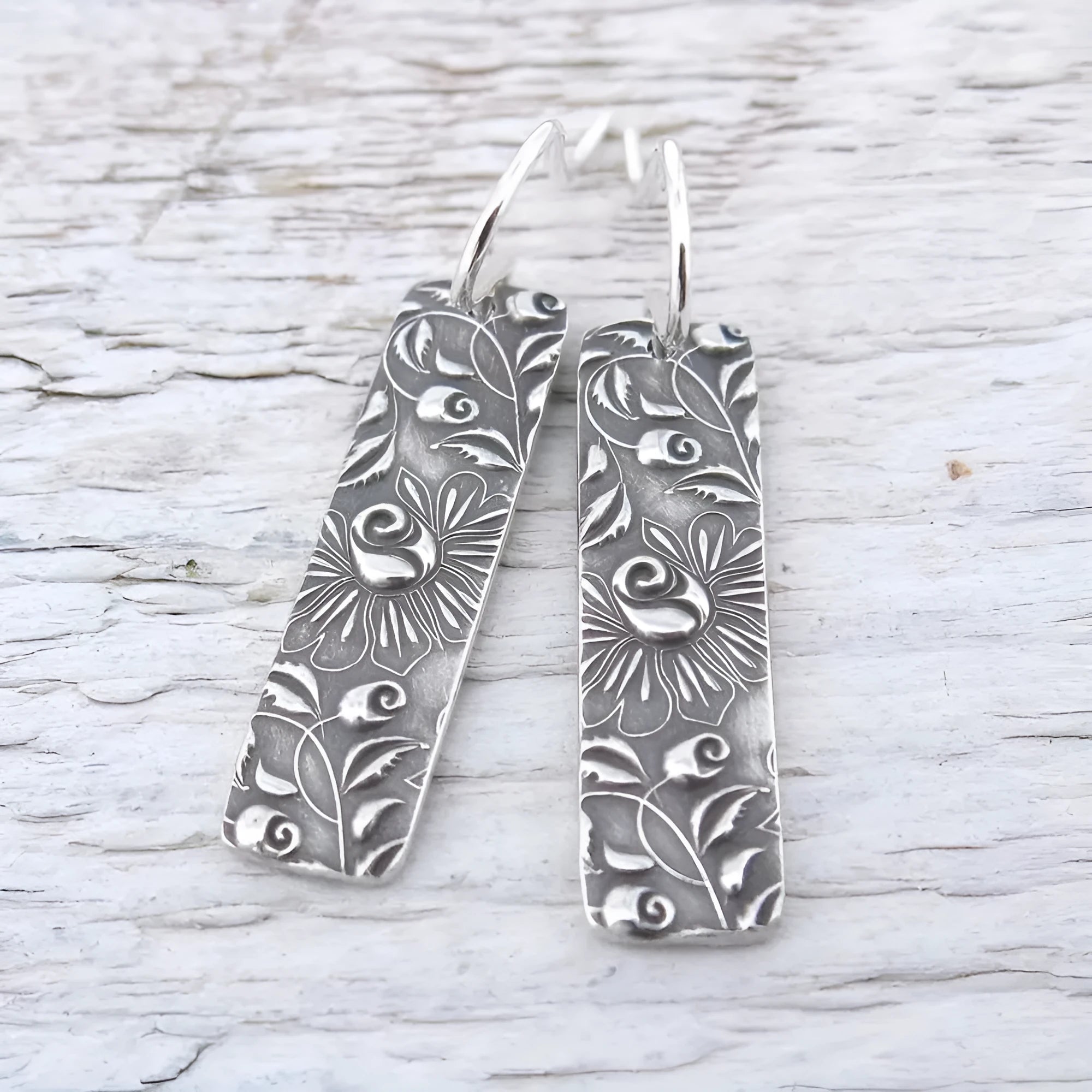 Silver retro geometric long strip carved vine earrings made from zinc alloy on a plain background