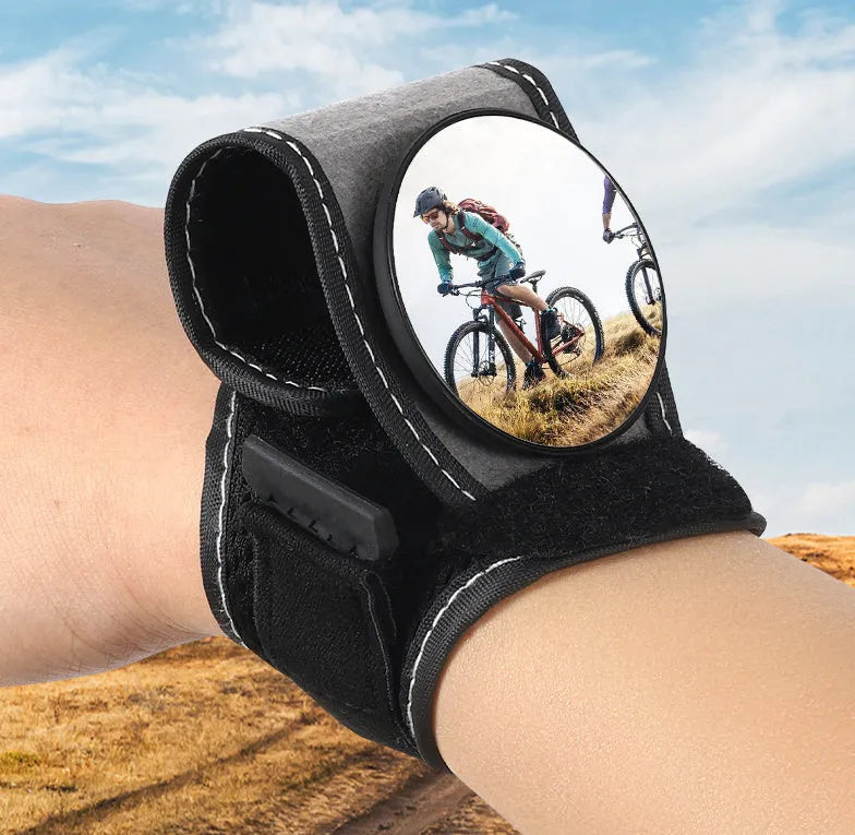 Black nylon wrist-mounted bicycle rear-view mirror shown on a cyclist's wrist.