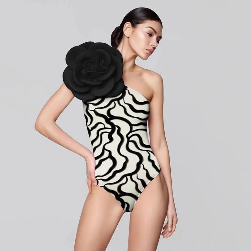 Form-fitting one-piece swimsuit with three-dimensional floral decoration on solid colour fabric.