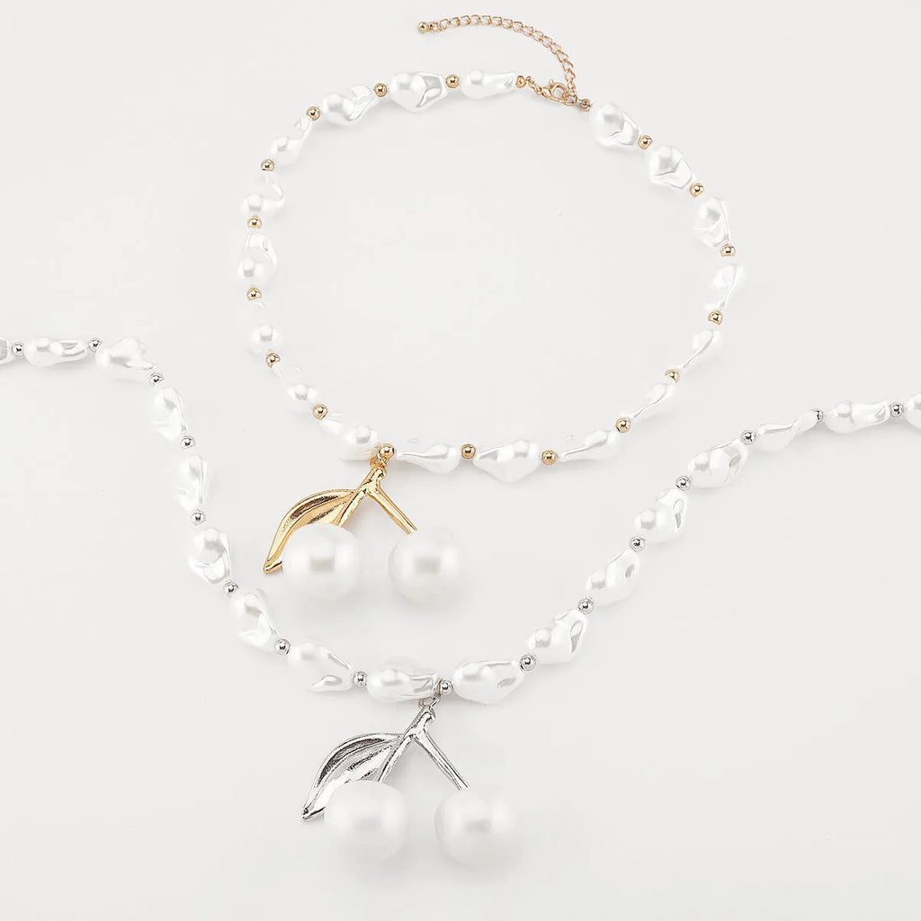 Women's gold alloy necklace with cherry fruit pendant and imitation pearl chain on white background.