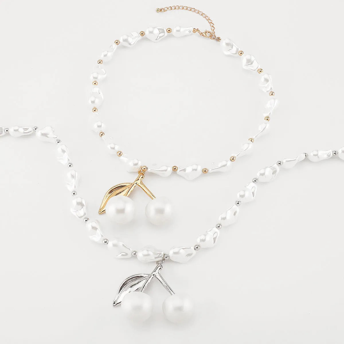 Women's gold alloy necklace with cherry fruit pendant and imitation pearl chain on white background.