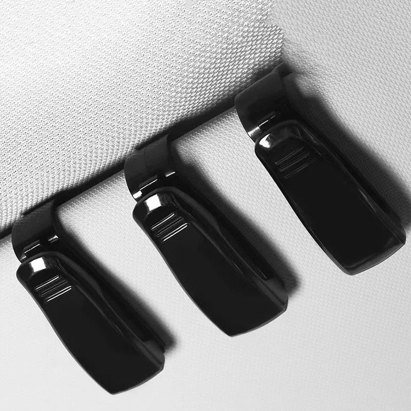 Black plastic clip for car sunshade holding a ticket and glasses
