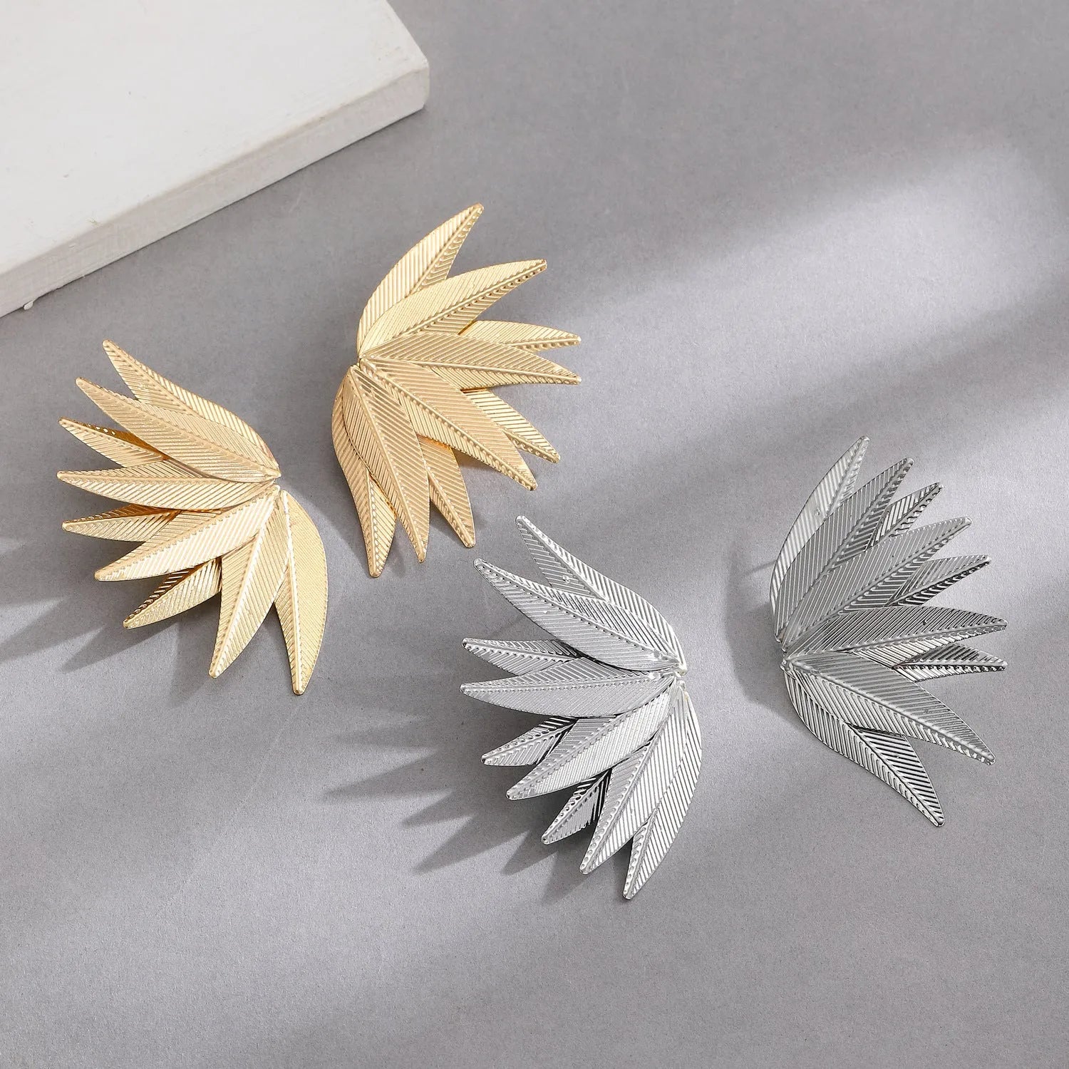 Gold and white leaf-shaped patch earrings made of alloy metal on a neutral background