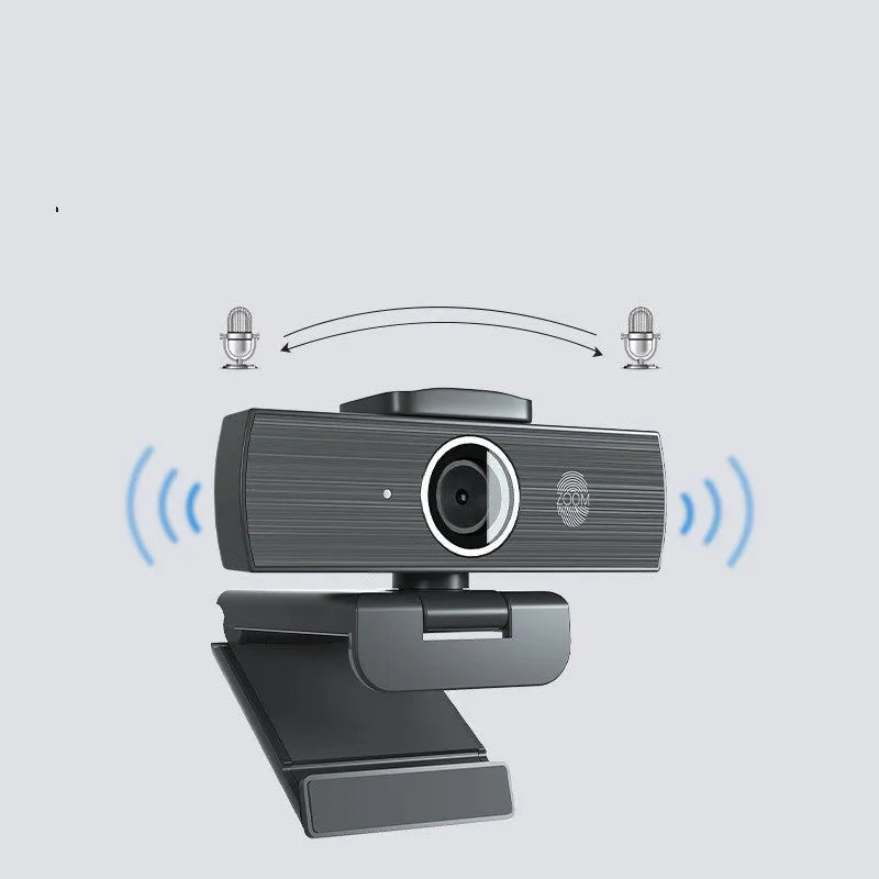Black USB computer webcam with magnetic privacy cover on a desk next to a laptop.