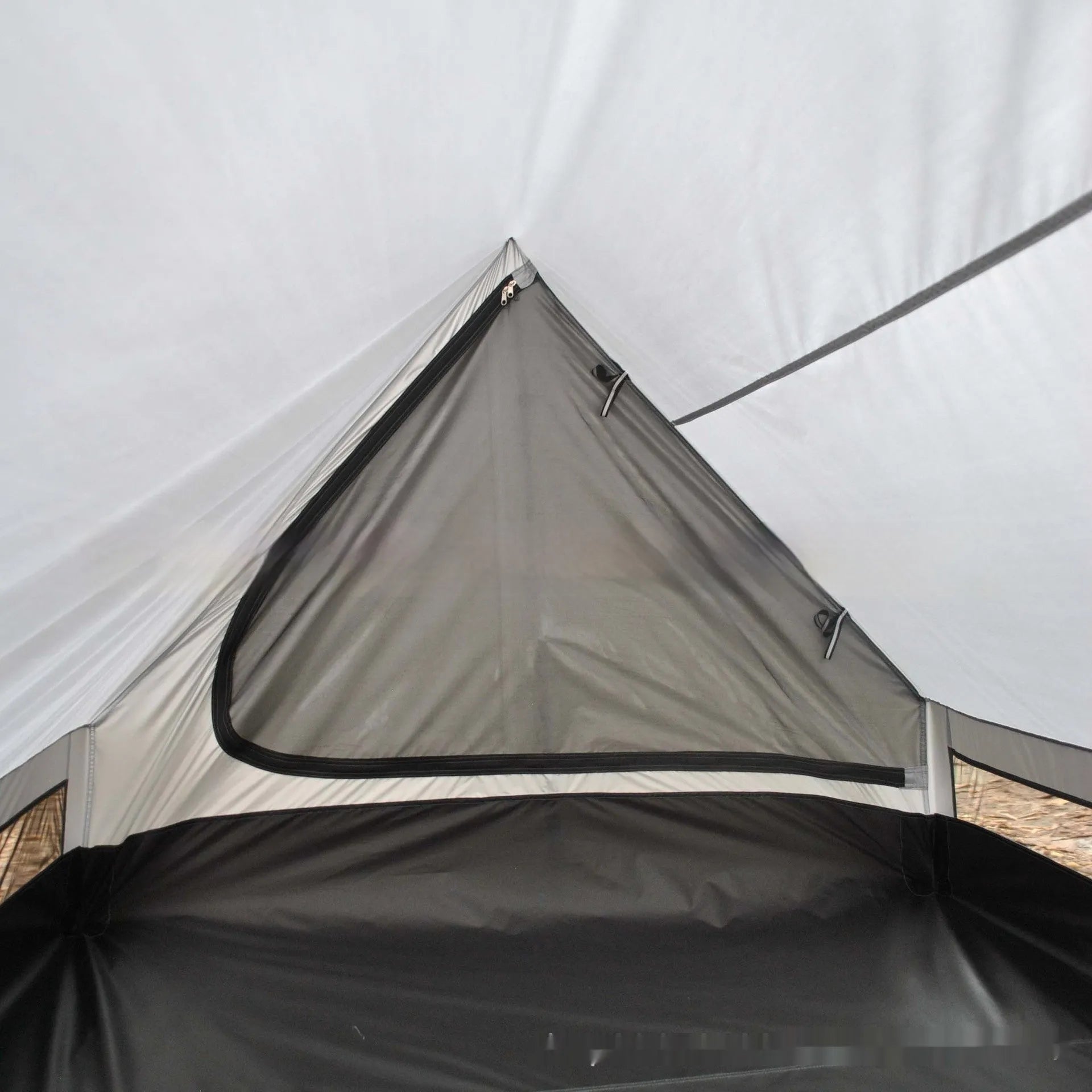 Brown A-line hiking tent set up with trekking poles in a forest clearing.