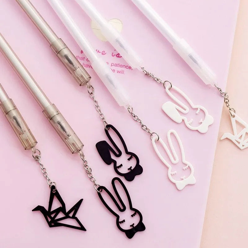 White gel pen with paper crane pendant and black gel pen with rabbit pendant on cap.