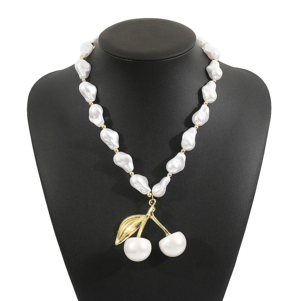 Women's gold alloy necklace with cherry fruit pendant and imitation pearl chain on white background.