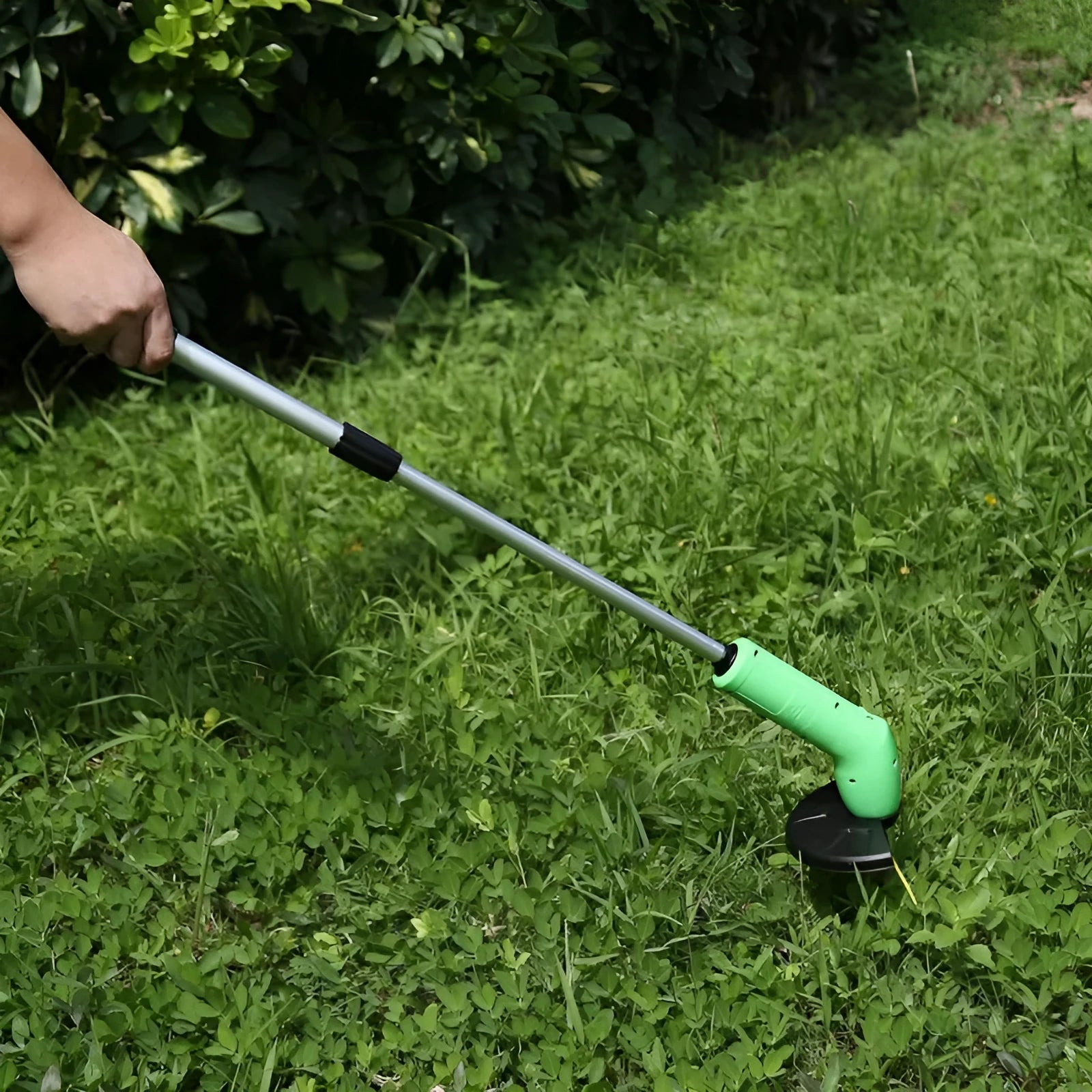 Cordless lawn trimmer with lightweight extension pole and protective debris shield on grass