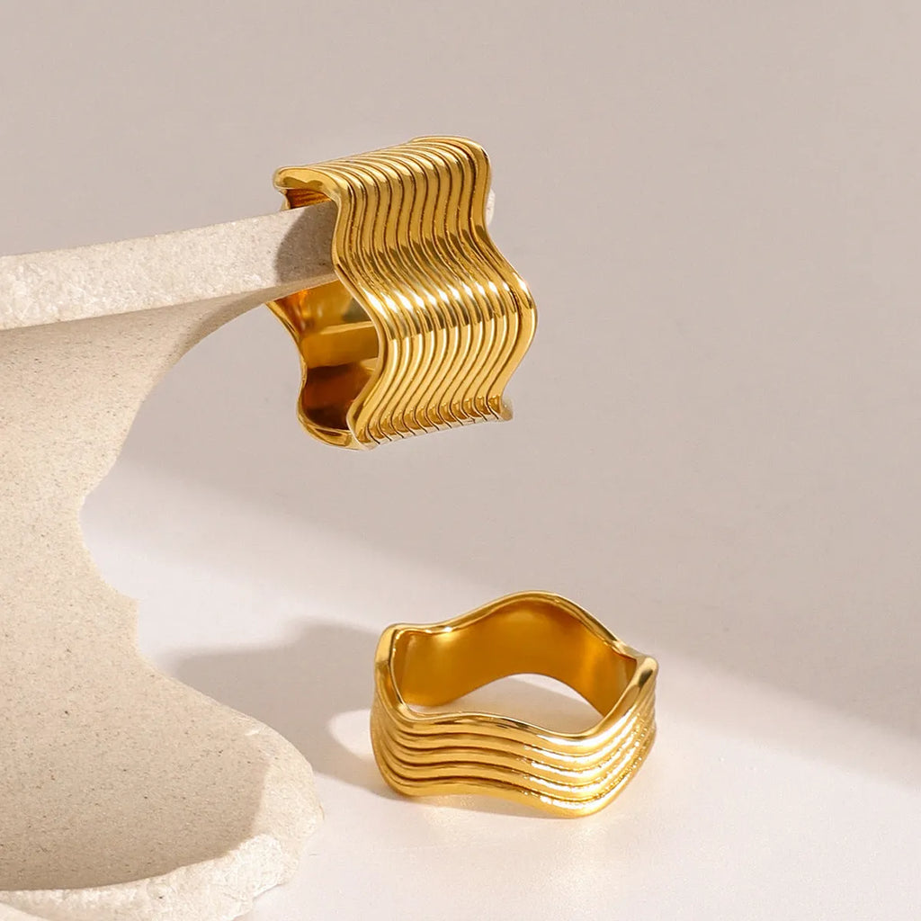 Stainless steel ring with a wide geometric wave design in a gold or silver finish.