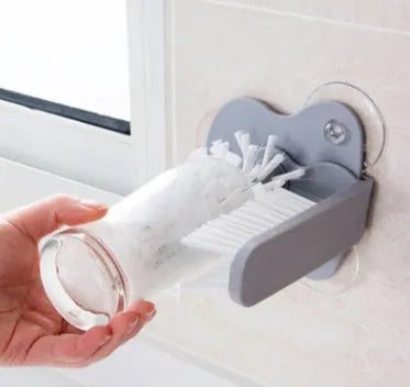 Grey suction cup brush with double-head design and two suction cups on a kitchen wall