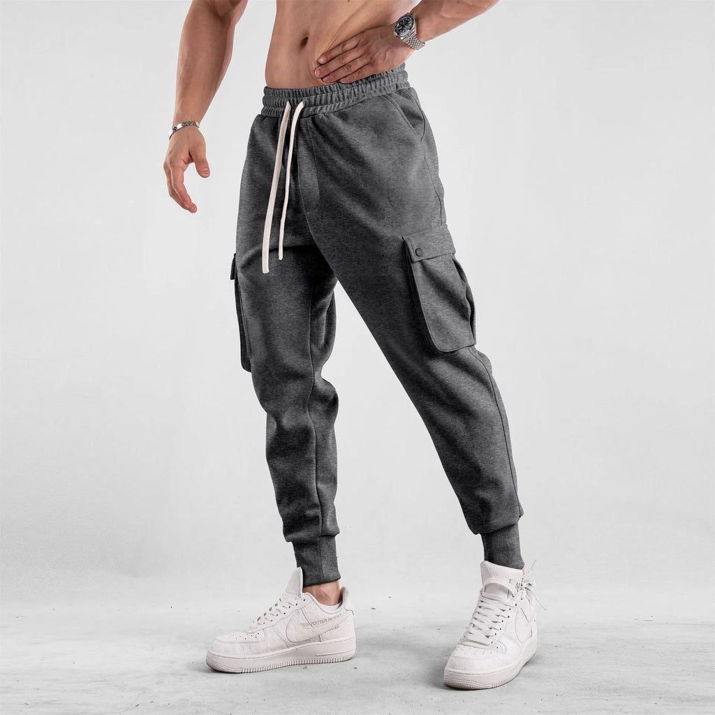 Men's loose fit beige cotton trousers with an ankle tie and multiple pockets on a man standing casually.