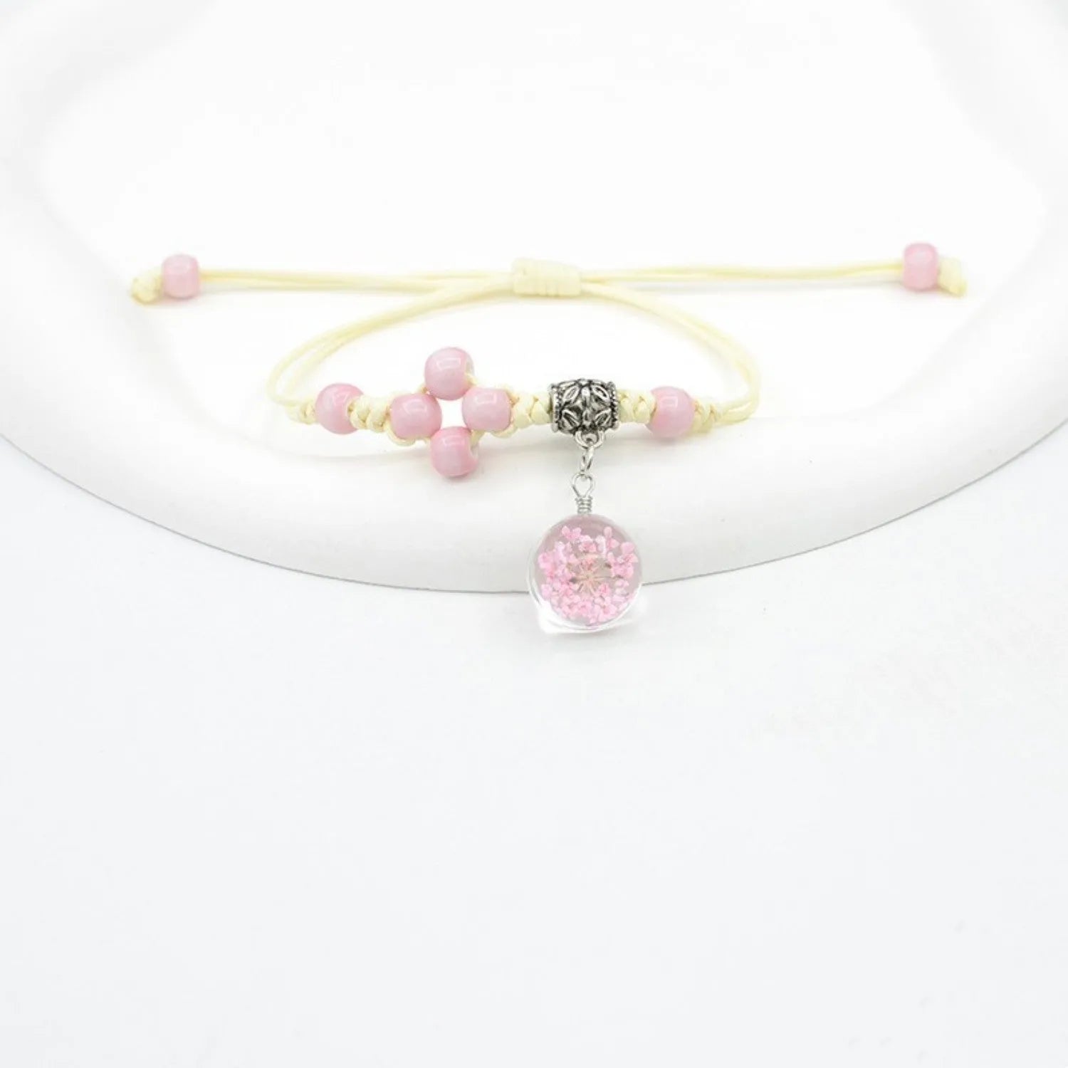 Close-up of a women's glass bracelet with large 1.4cm beads containing dried flowers and a hand-woven lace pattern.