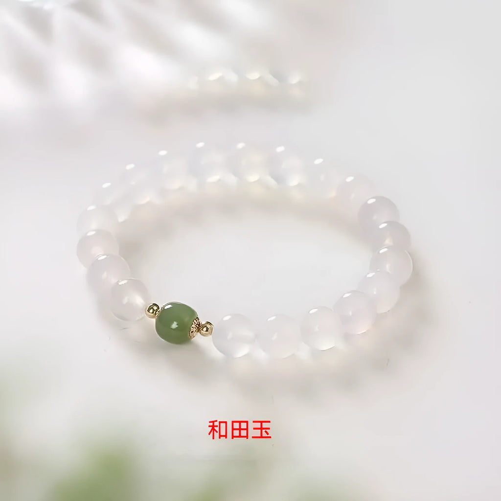 Handmade white agate and cinnabar bracelet with letter charms on a wrist.