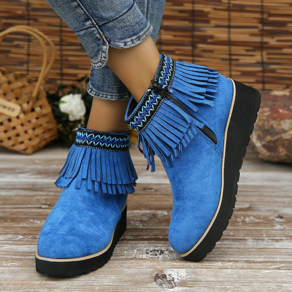 Women's ankle boot in suede with wedge heel, side zipper, and tassel detail on a dark background.