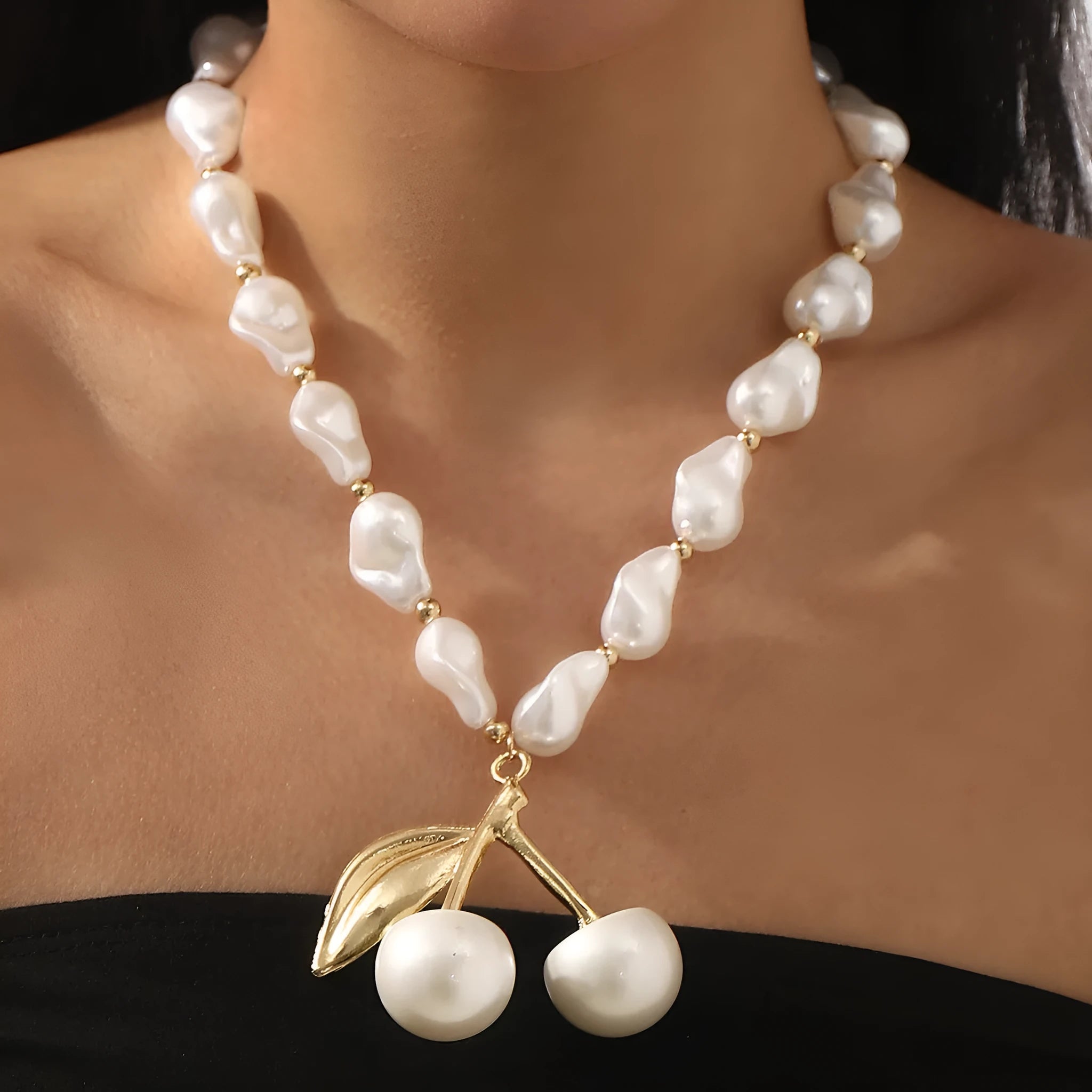 Women's gold alloy necklace with cherry fruit pendant and imitation pearl chain on white background.