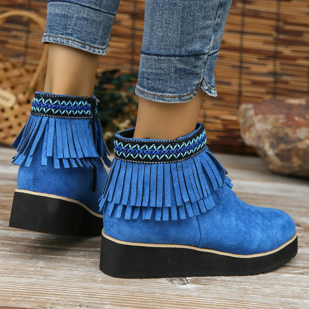 Women's ankle boot in suede with wedge heel, side zipper, and tassel detail on a dark background.