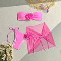 Women's pink tube top swimsuit with 3D flower tie, matching bottoms, and a skirt laid flat.