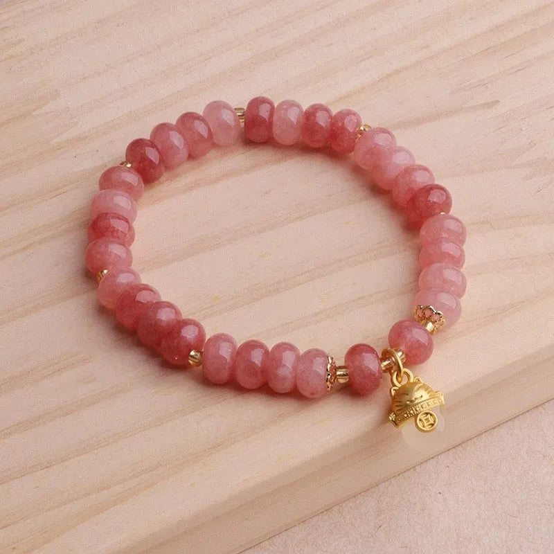 Women's handmade strawberry quartz Lucky Cat bracelet on a neutral background