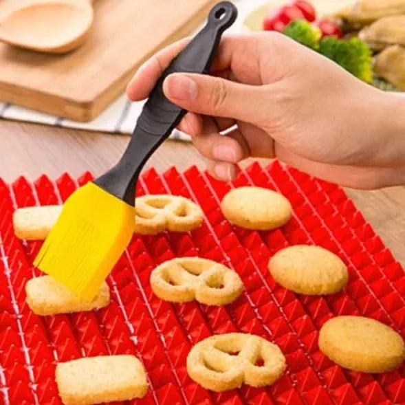 Red non-stick silicone pyramid cooking mat with grid on a baking tray for oven or BBQ use