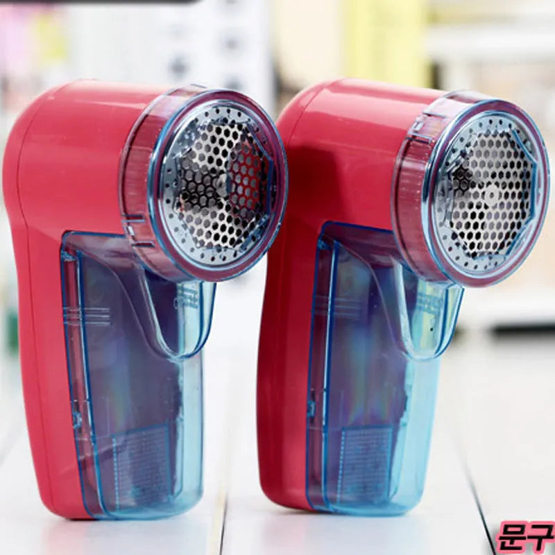 Compact white electric lint remover for clothing on a table next to a grey sweater.