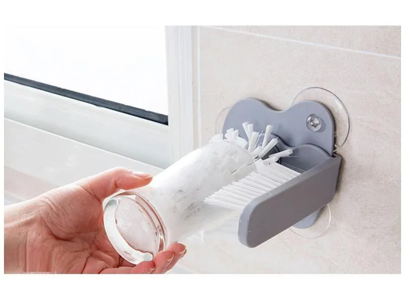 Grey suction cup brush with double-head design and two suction cups on a kitchen wall