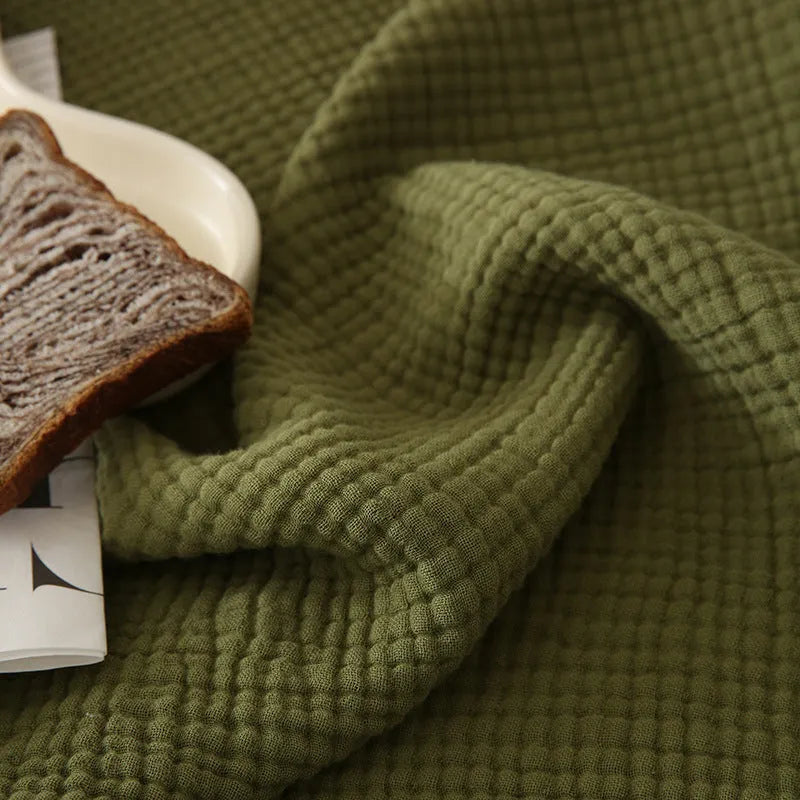 Four-layer gauze tassel cotton blanket in avocado green colour laid flat.