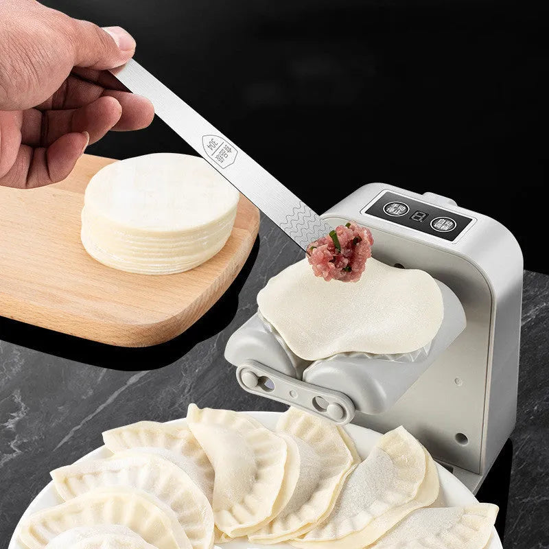 White automatic electric dumpling maker machine on a kitchen counter with USB cable and accessories