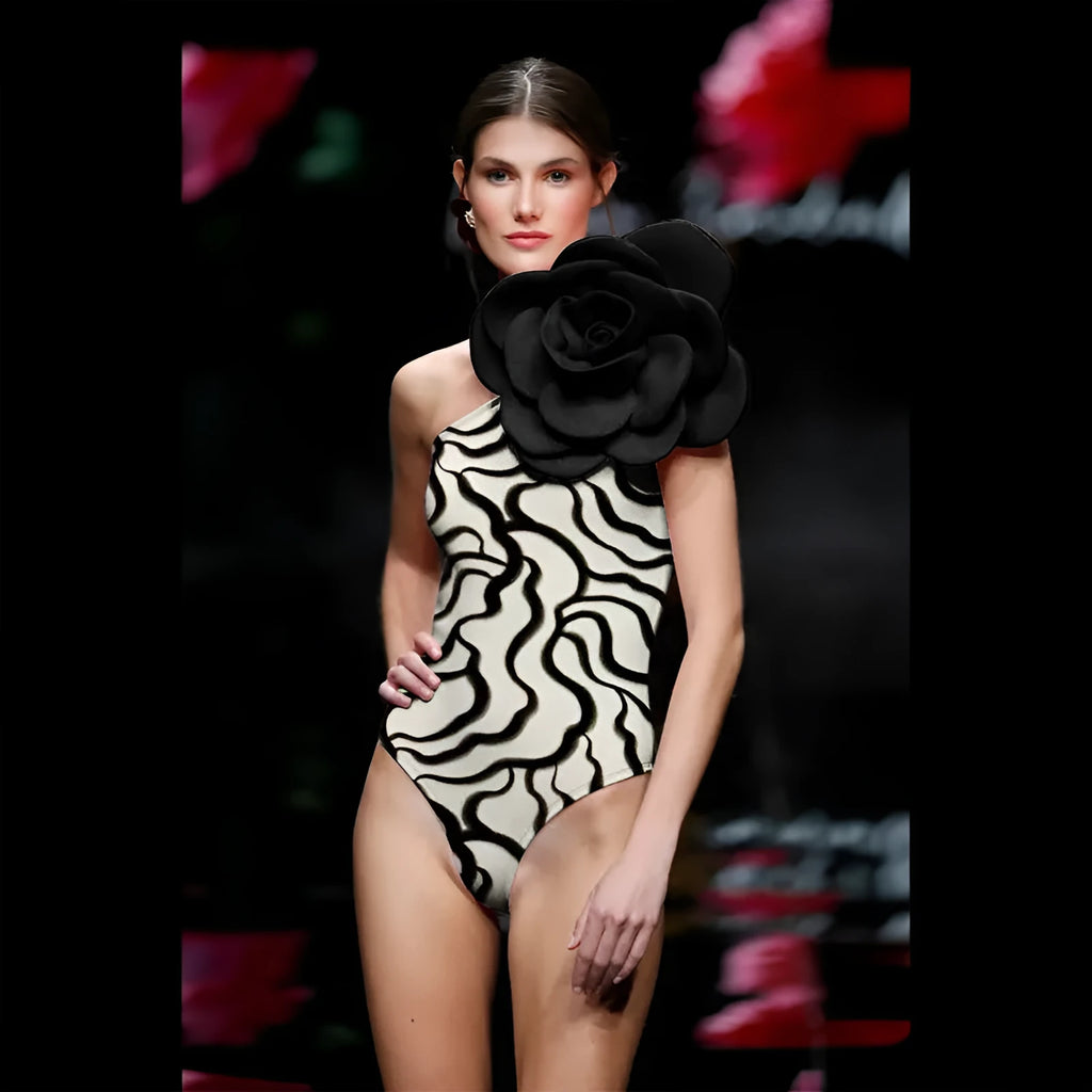 Form-fitting one-piece swimsuit with three-dimensional floral decoration on solid colour fabric.