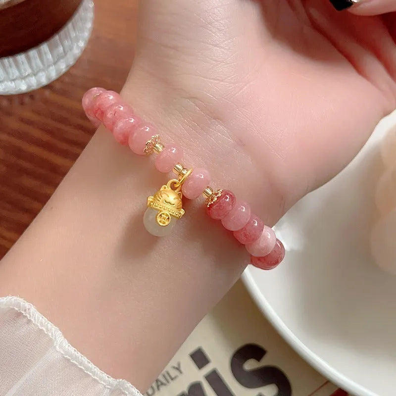 Women's handmade strawberry quartz Lucky Cat bracelet on a neutral background