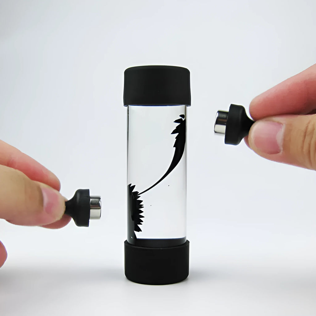 Magnetic fluid toy in a glass bottle with red ferrofluid and two black magnets on a white surface