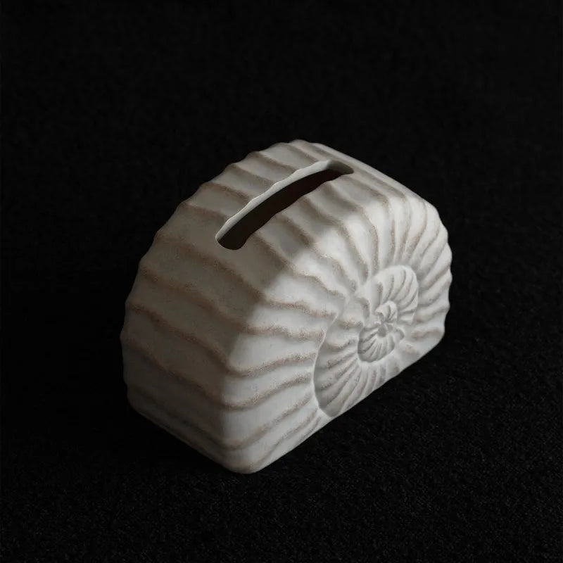 White conch shell shaped resin cover for a rectangular tissue box with a slot for tissue dispensing.
