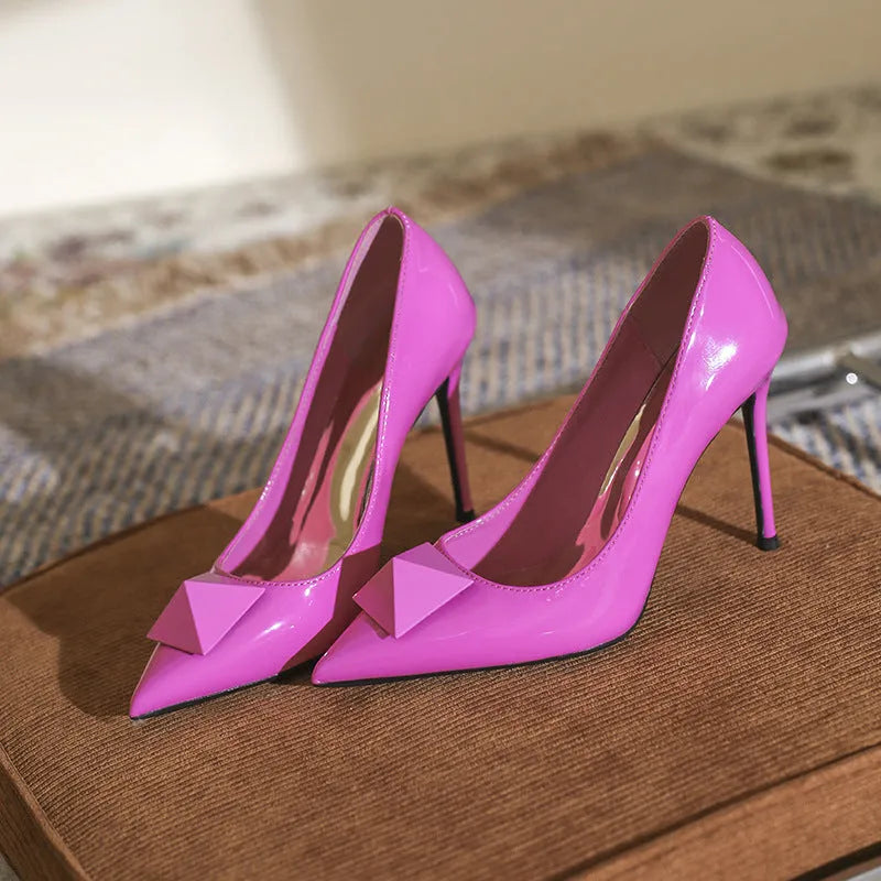 Pink women's patent leather pointed toe stiletto high heels with a buckle, on a white background.