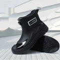 Pair of solid colour PVC rain boots with flat heel and low tube, round toe, visible sewing thread detail