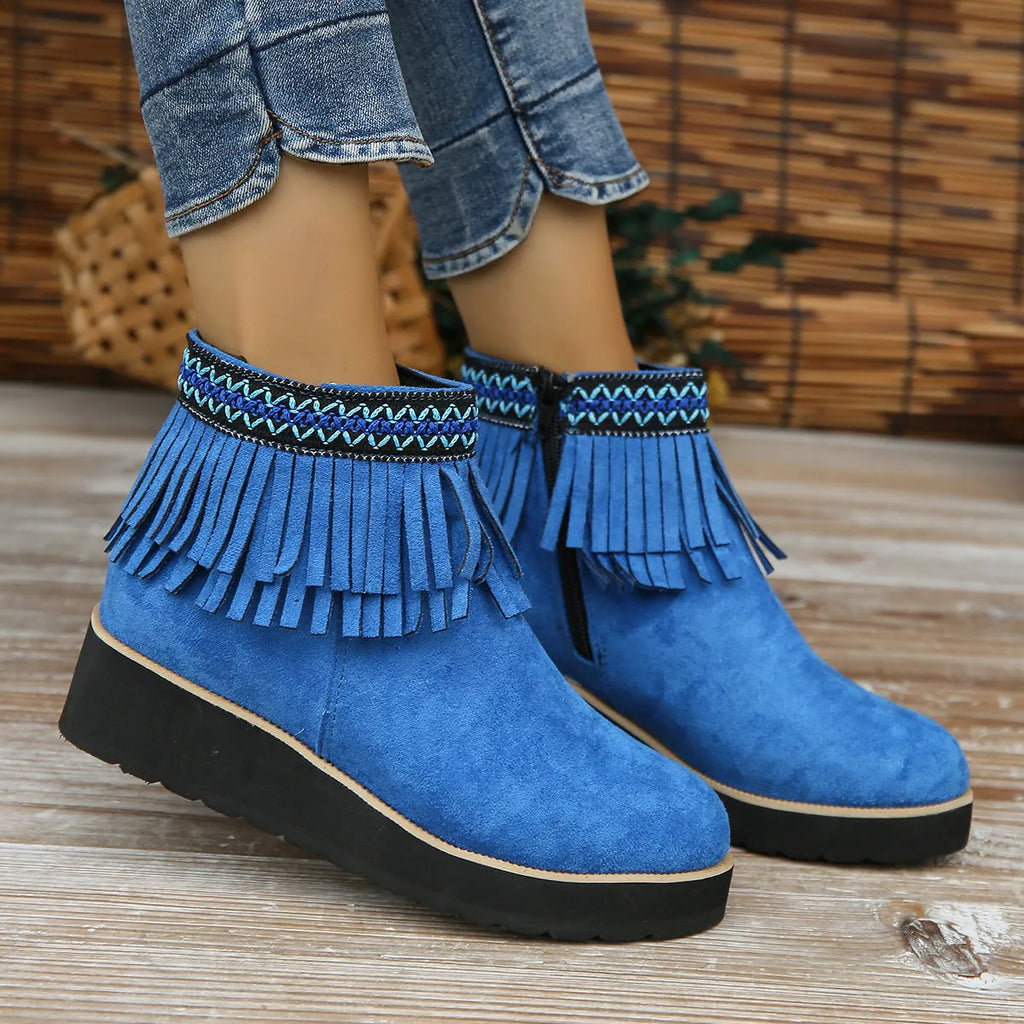 Women's ankle boot in suede with wedge heel, side zipper, and tassel detail on a dark background.