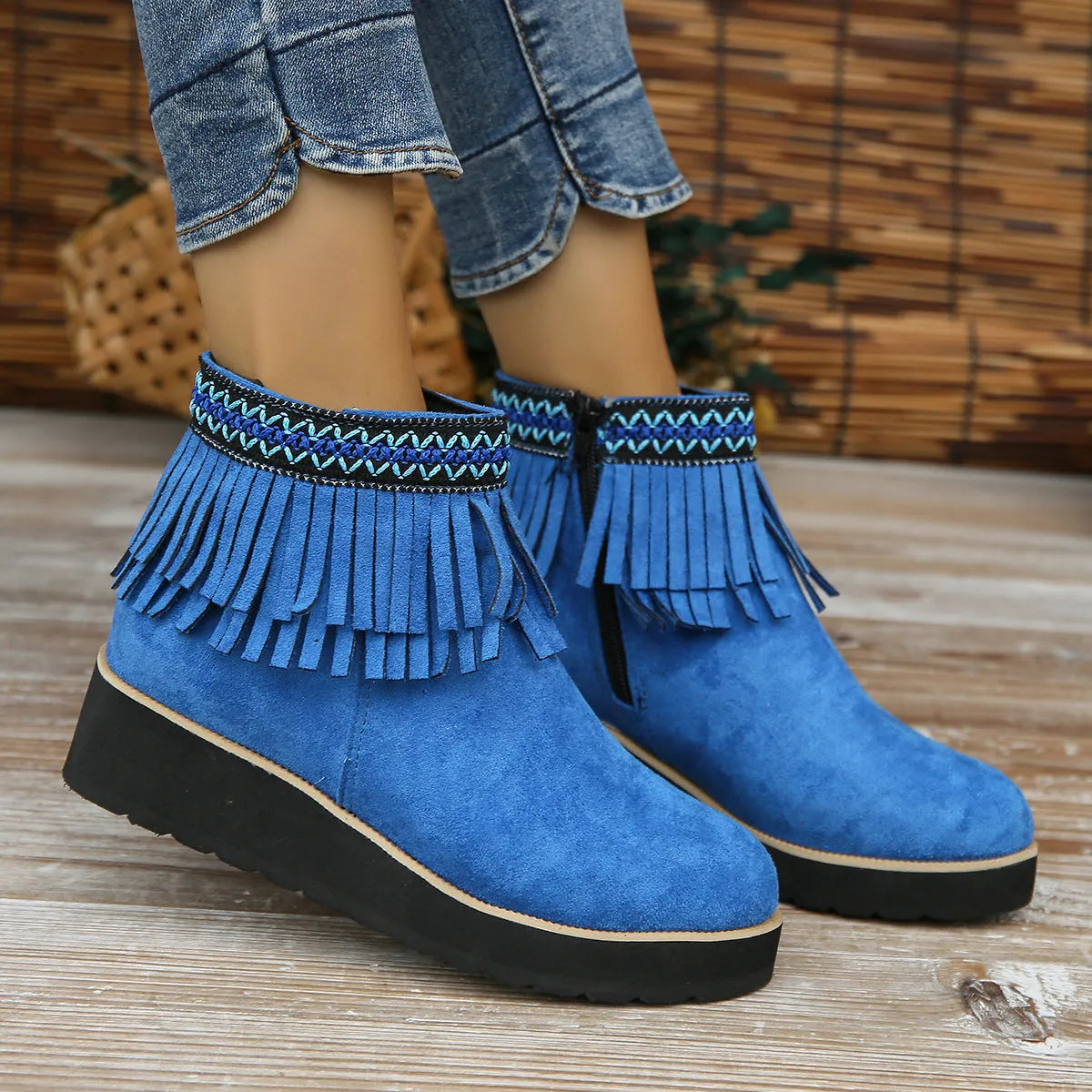 Women's ankle boot in suede with wedge heel, side zipper, and tassel detail on a dark background.