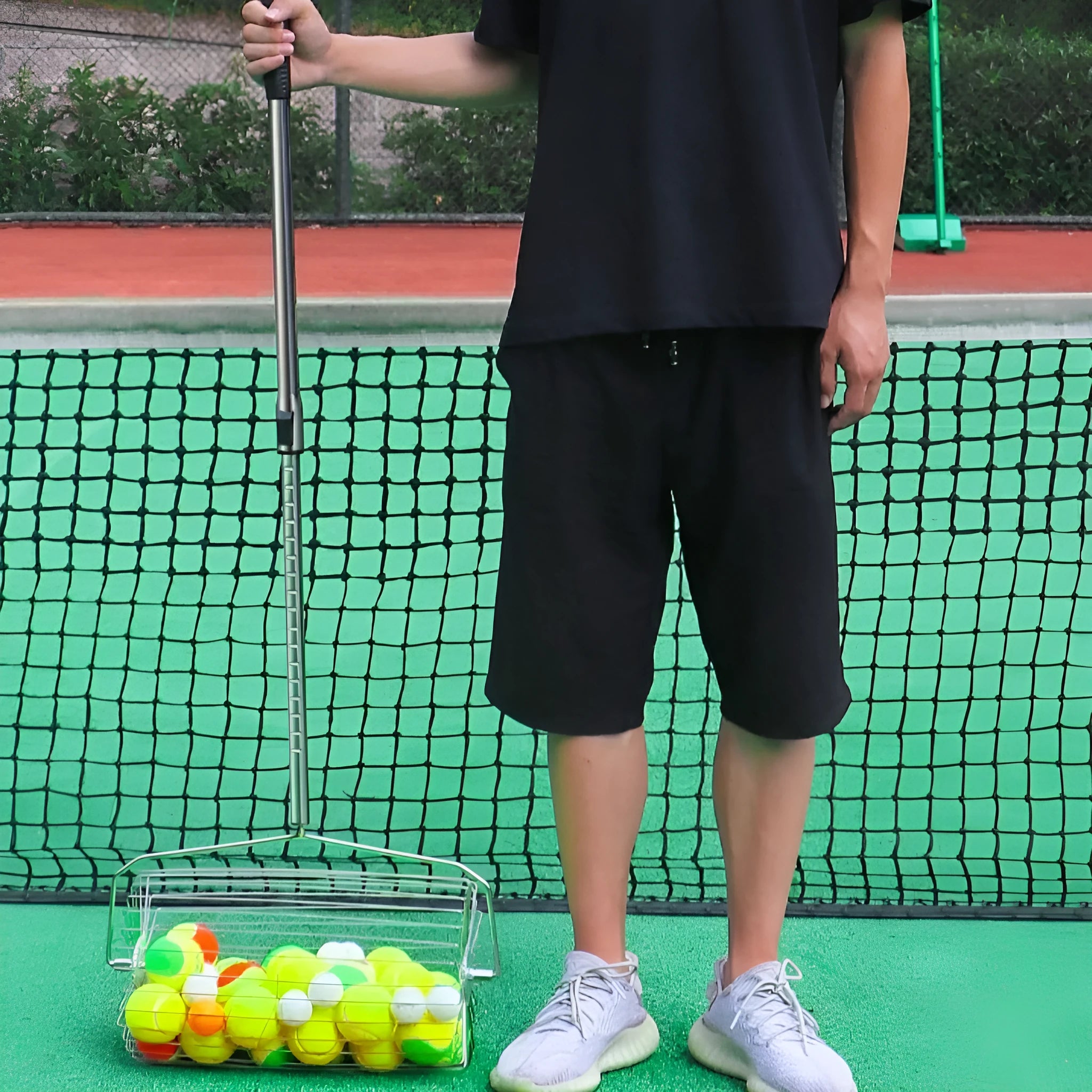 Stainless steel manual roller tennis ball picker on a court surface.