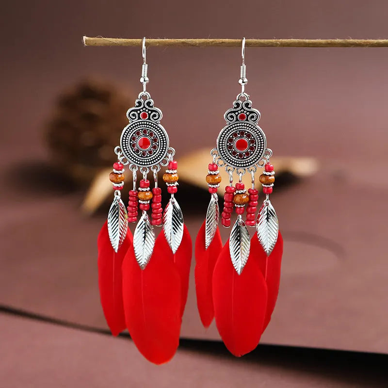 Close-up of a pair of bohemian feather and leaf pattern drop earrings in a light pink electroplated finish.