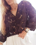 Loose V-neck lace cardigan with white three-dimensional floral decorations on a black background.