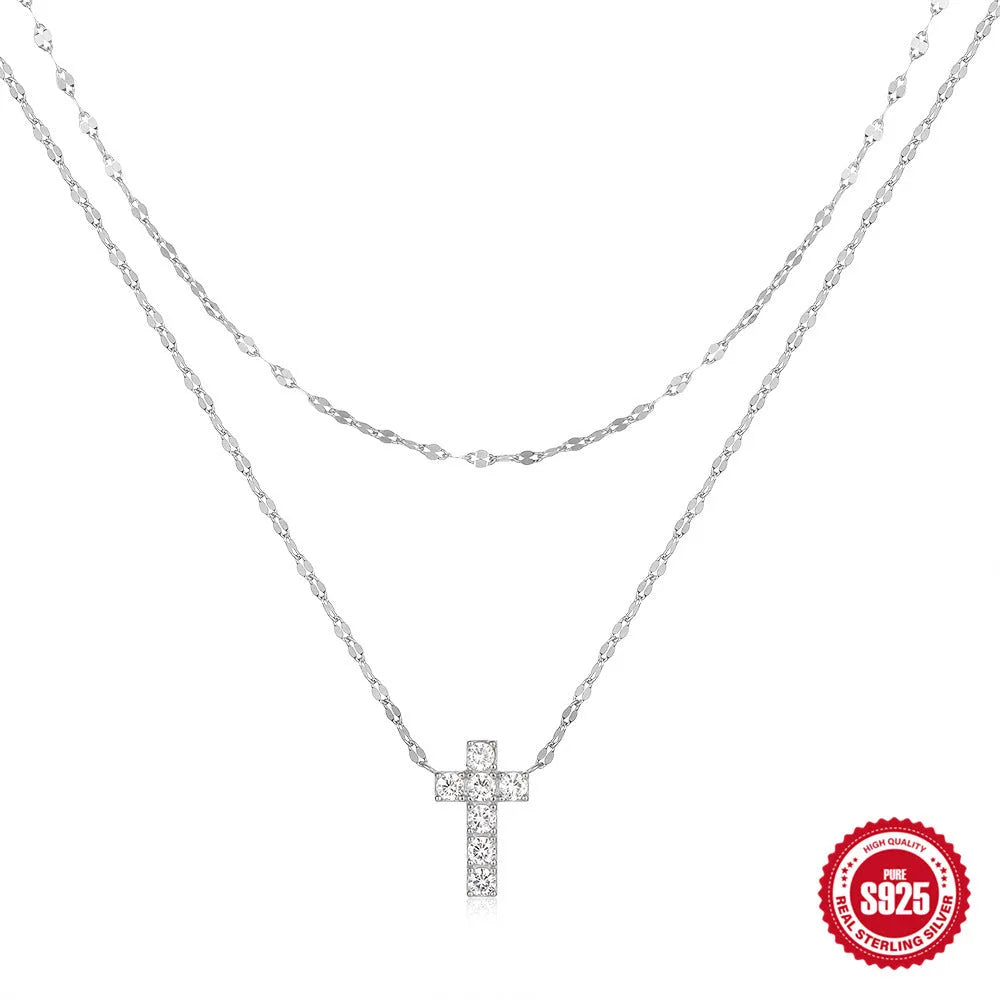 Close-up of a sterling silver double-layer cross pendant necklace with twin diamond accents on a clavicle chain.