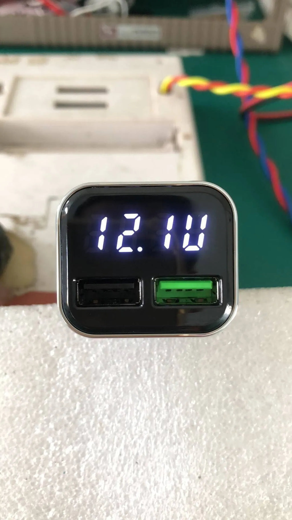 Black car charger with LCD display showing voltage reading, dual USB ports, PC+ABS construction