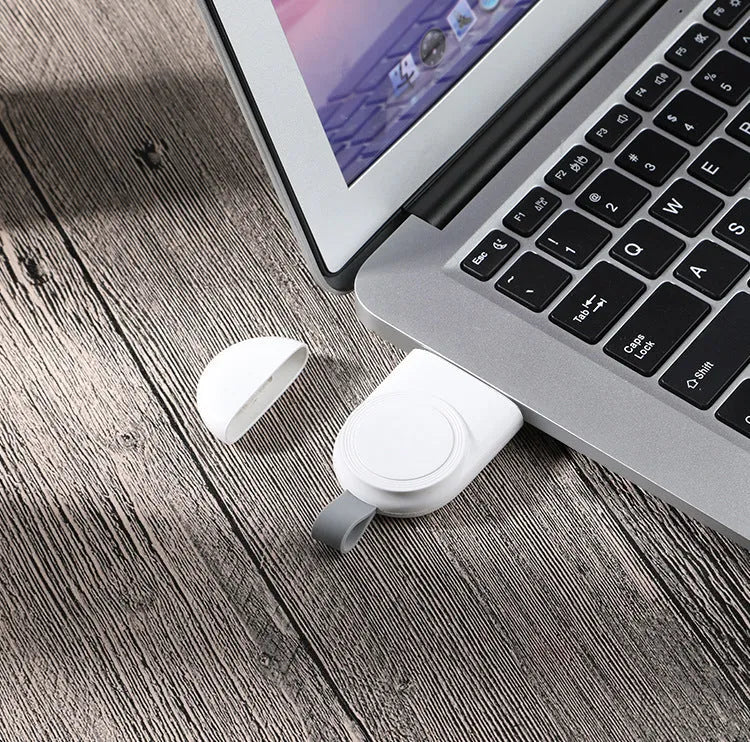 Portable Apple Watch wireless charging dock in white on a wooden table, with USB cable attached.