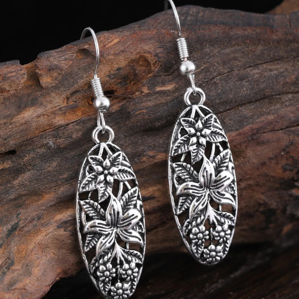 Pair of silver-tone retro hollowed out long water droplet drop earrings on light background