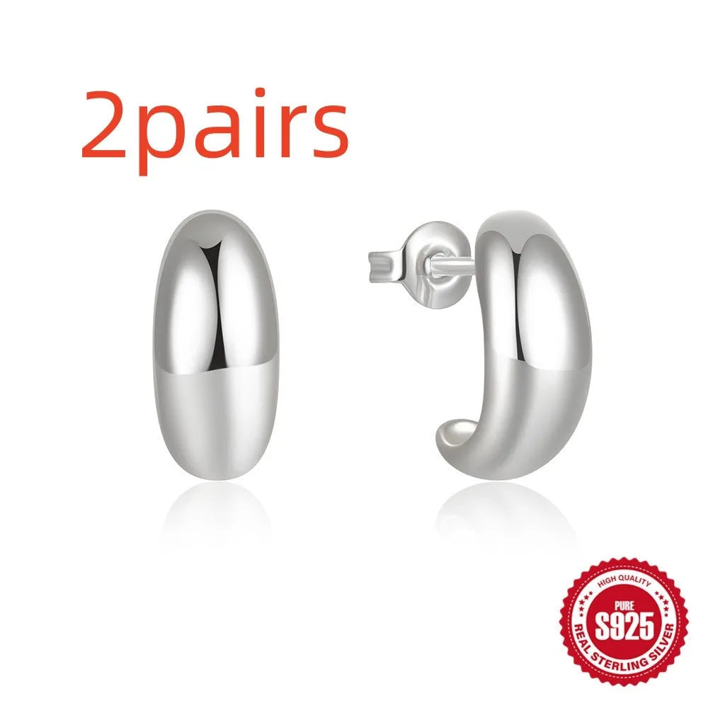 Glossy gold and silver tone C-shaped sterling silver stud earrings on a plain background.
