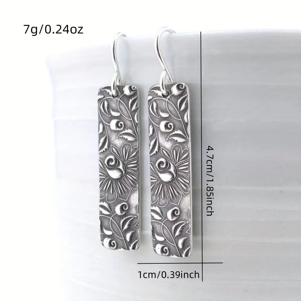 Silver retro geometric long strip carved vine earrings made from zinc alloy on a plain background