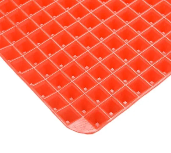 Red non-stick silicone pyramid cooking mat with grid on a baking tray for oven or BBQ use