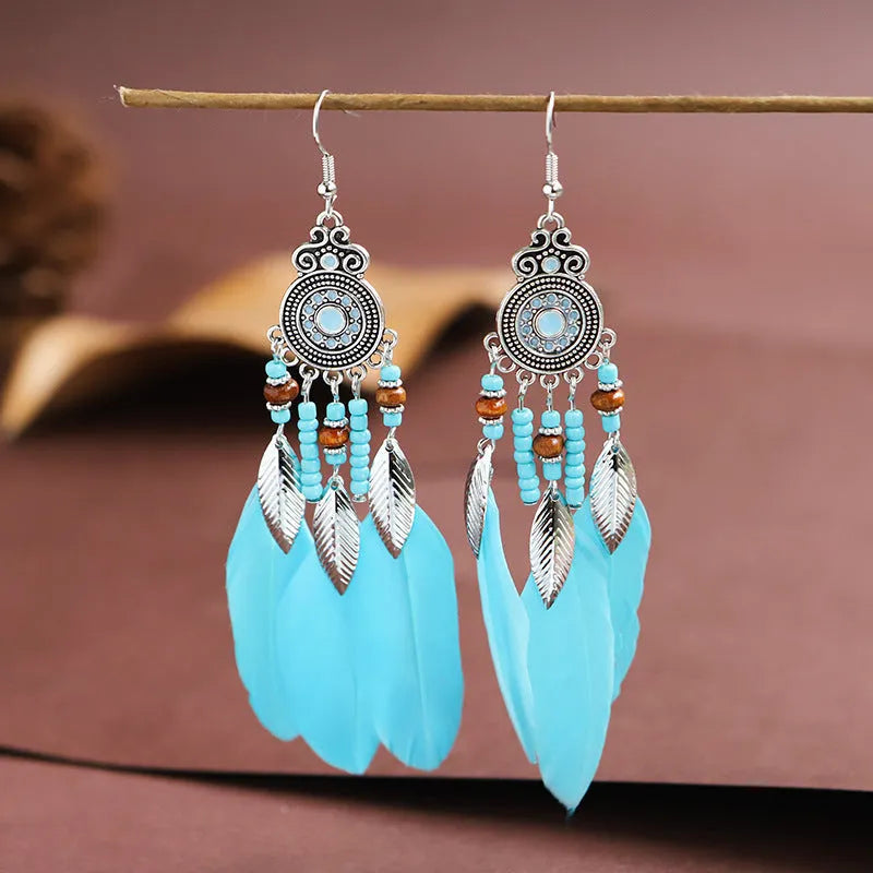Close-up of a pair of bohemian feather and leaf pattern drop earrings in a light pink electroplated finish.