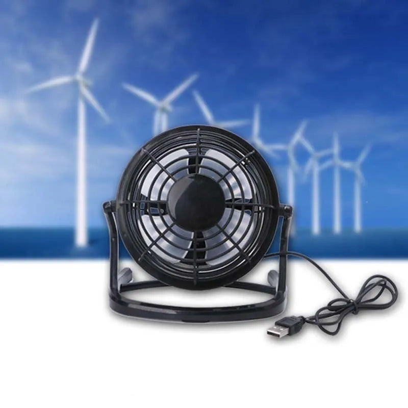 Small black USB desk fan with adjustable head on a wooden desk next to a laptop