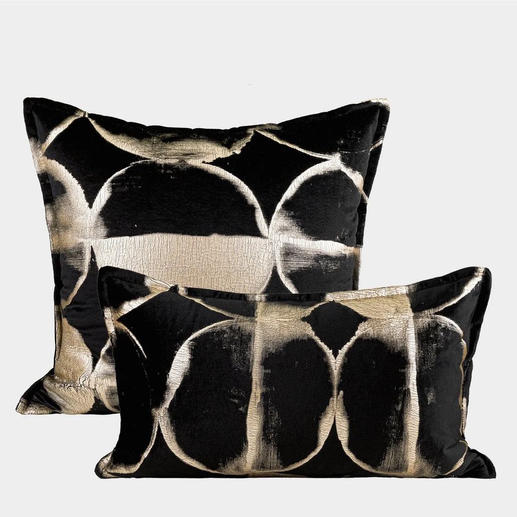 Black and gold abstract patterned decorative flannel cushion on a grey sofa.