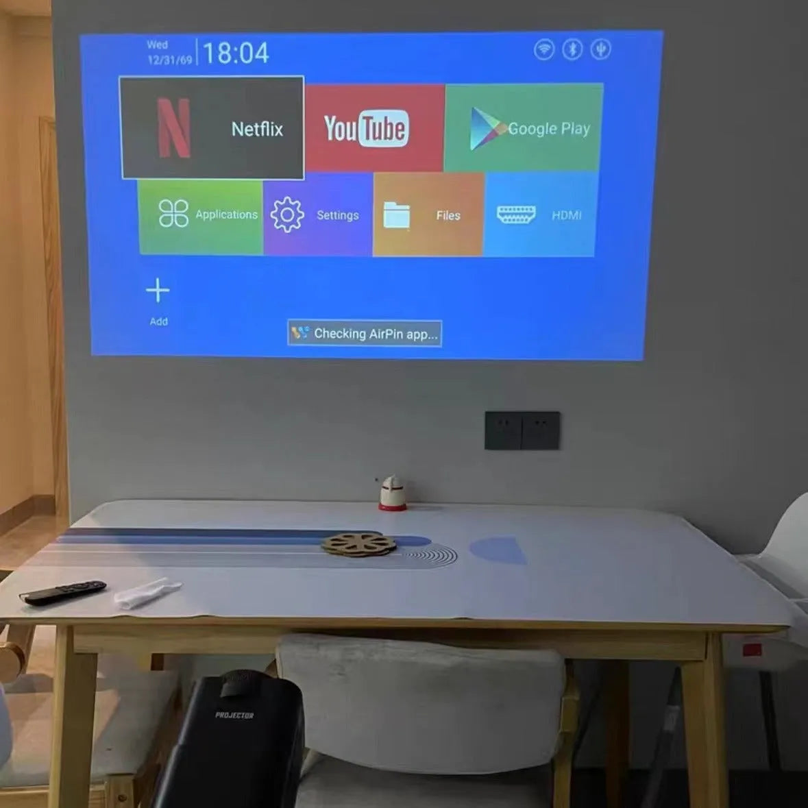 A wireless home projector with a carrying handle, displaying a bright game or movie on a wall.